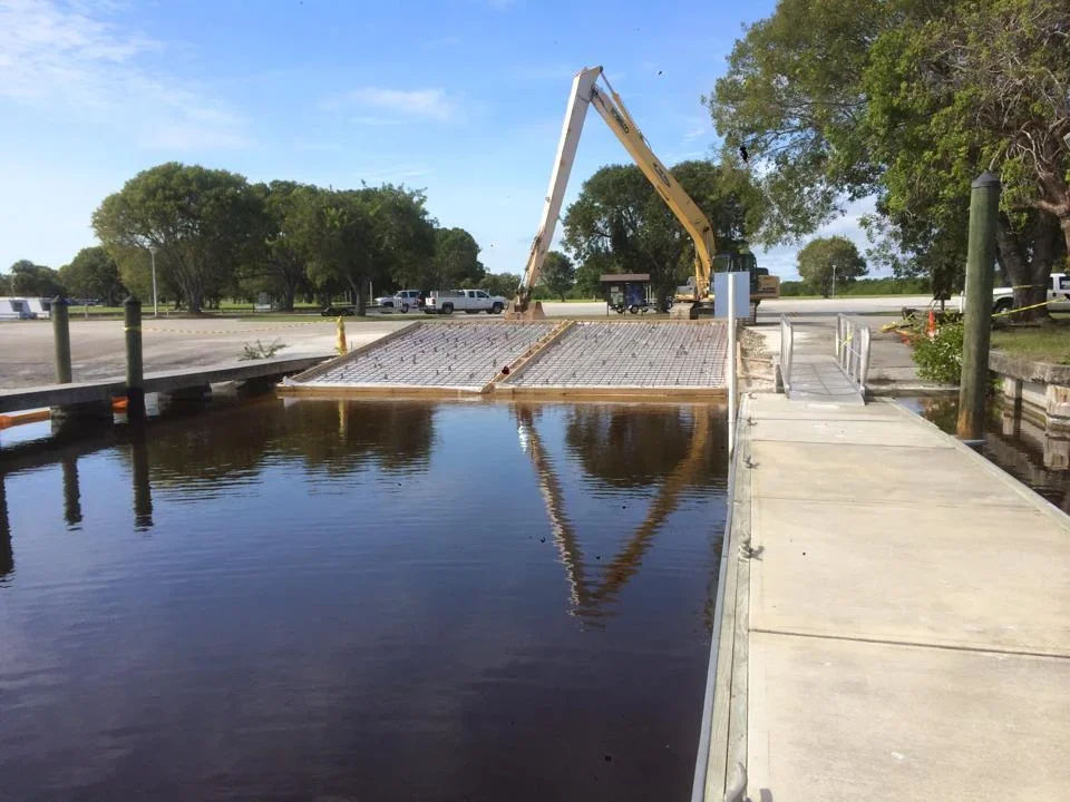 Concrete dock with metal grating deck installed along waterfront canal with equipment and trees