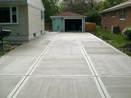 Gray concrete driveway with white control joints leading to garage