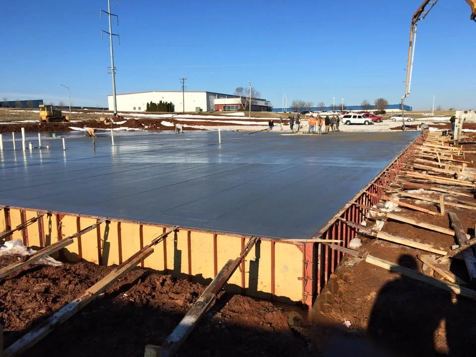 Fresh concrete foundation pour with yellow formwork and white concrete slab at commercial construction site