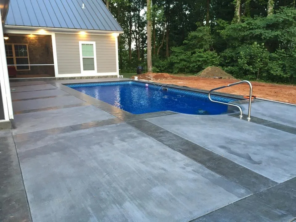 Stamped concrete pool deck with in-ground pool and modern pool house at dusk