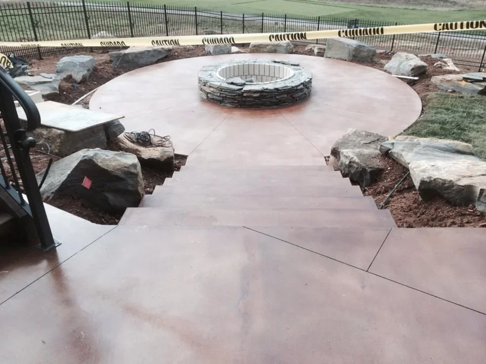 Circular concrete patio with central stone fire pit and decorative boulders