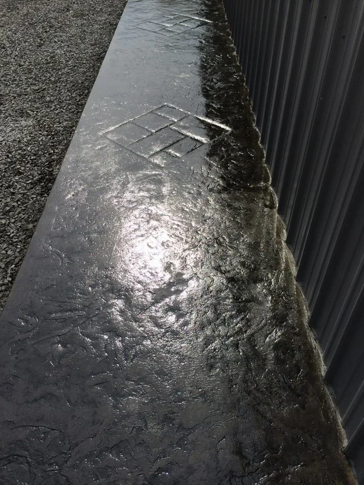 Wet concrete apron with diamond-pattern drainage grate near metal building wall