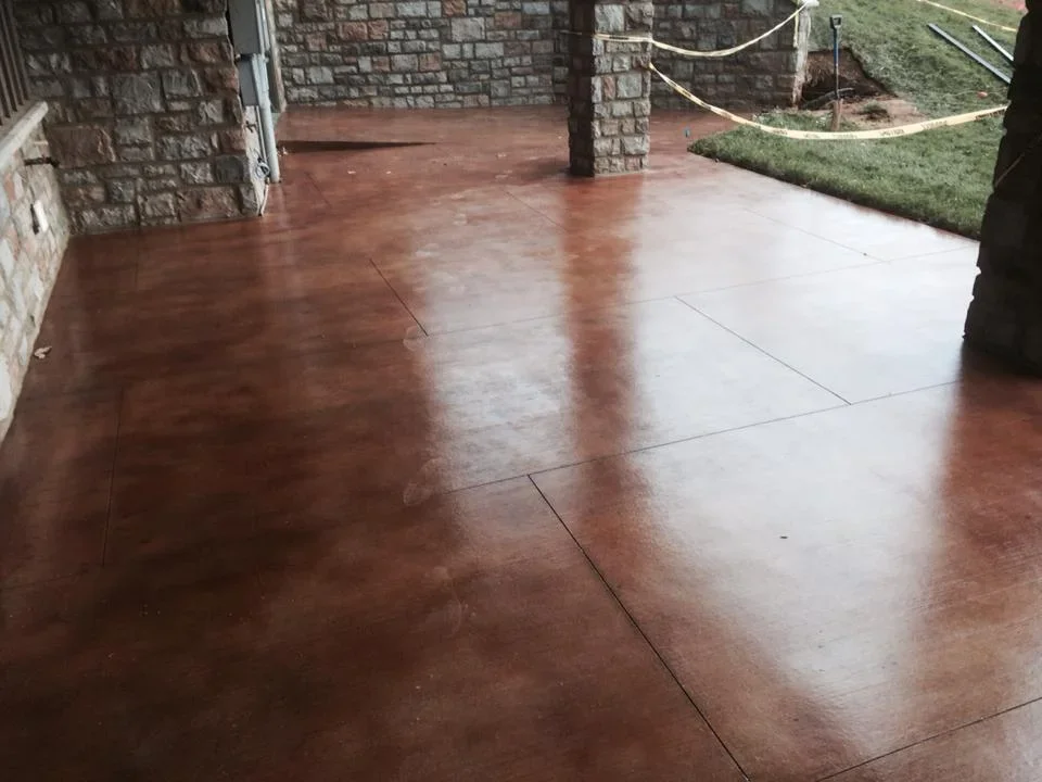 Stained concrete patio with reddish-brown finish and control joints near stone house