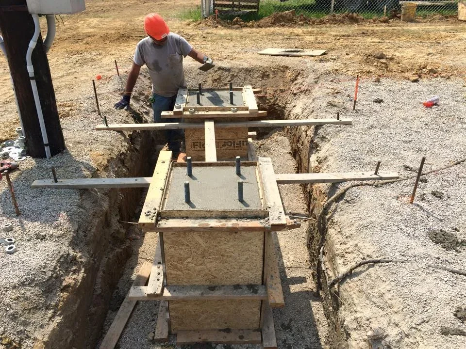 Worker in hard hat preparing concrete foundation forms in excavated trenches with wooden bracing