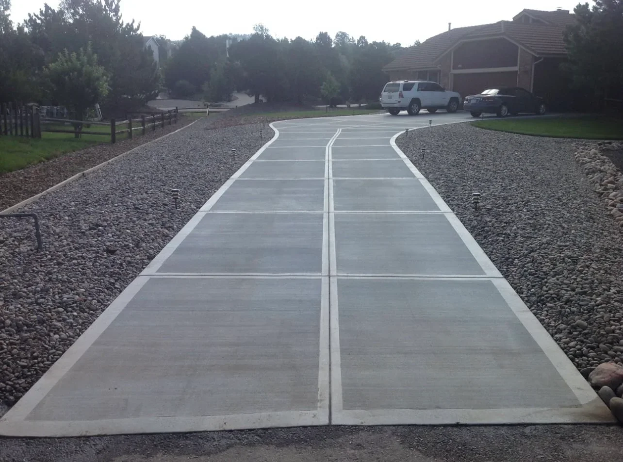 Curved concrete driveway with white border leading to garage and parked vehicles