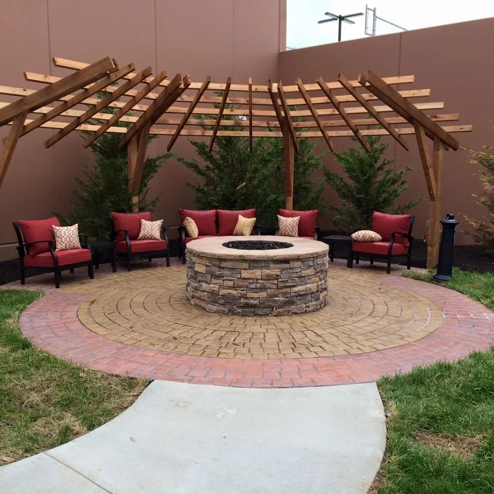 Circular paver patio with stone fire pit, wooden pergola, and red seating
