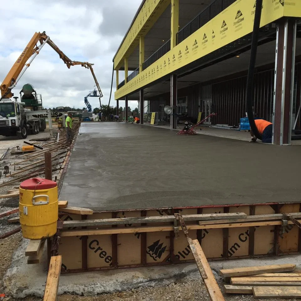 Finished concrete pad at commercial warehouse with yellow building and equipment in background