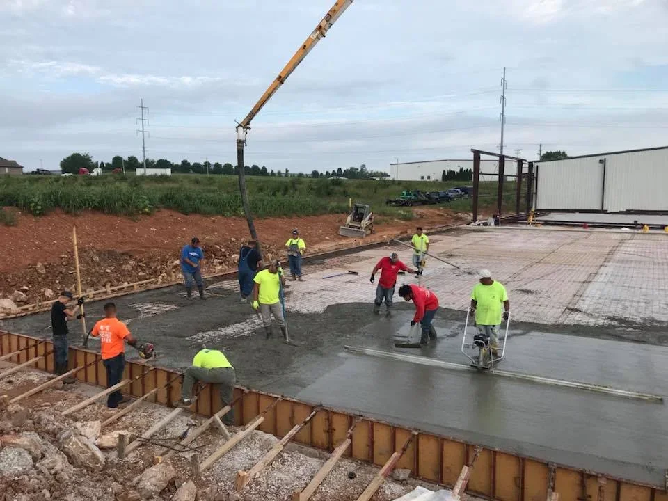 Concrete crew finishing large commercial concrete pad with pump truck and crane on-site