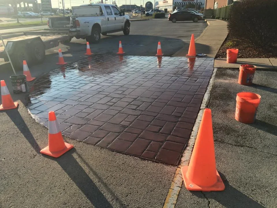 Dark brown decorative concrete pavers installed in commercial parking lot with safety cones